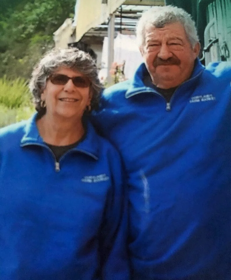 Man and woman standing next to each other in front of a truck, both wearing blue jackets