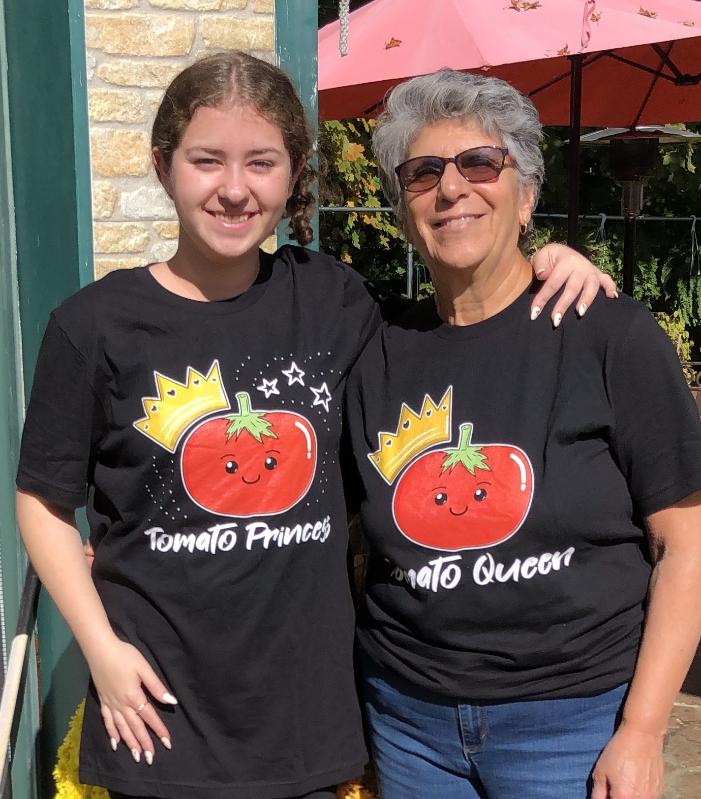Two women standing next to each other wearing matching black t-shirts with the words "" and "Queen" printed on them