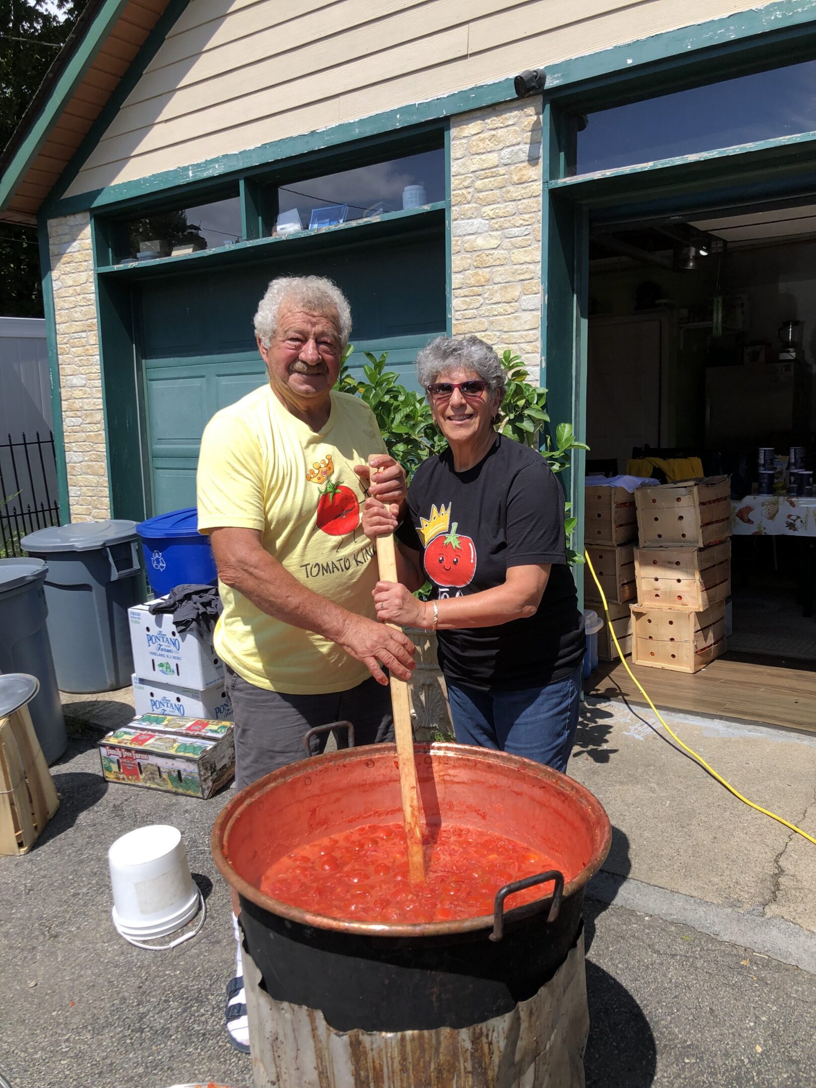 Man and woman standing next to each other in front of a large pot filled with tomato sauce