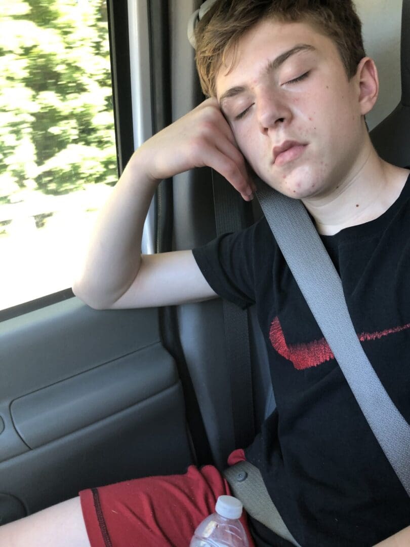 Boy sleeping in the back seat of a car, wearing a seat belt and holding a bottle in his hand