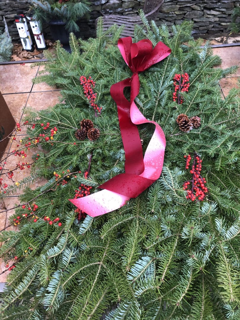 Christmas wreath with a red ribbon tied around it, adorned with leaves, fruits, and other decorative items