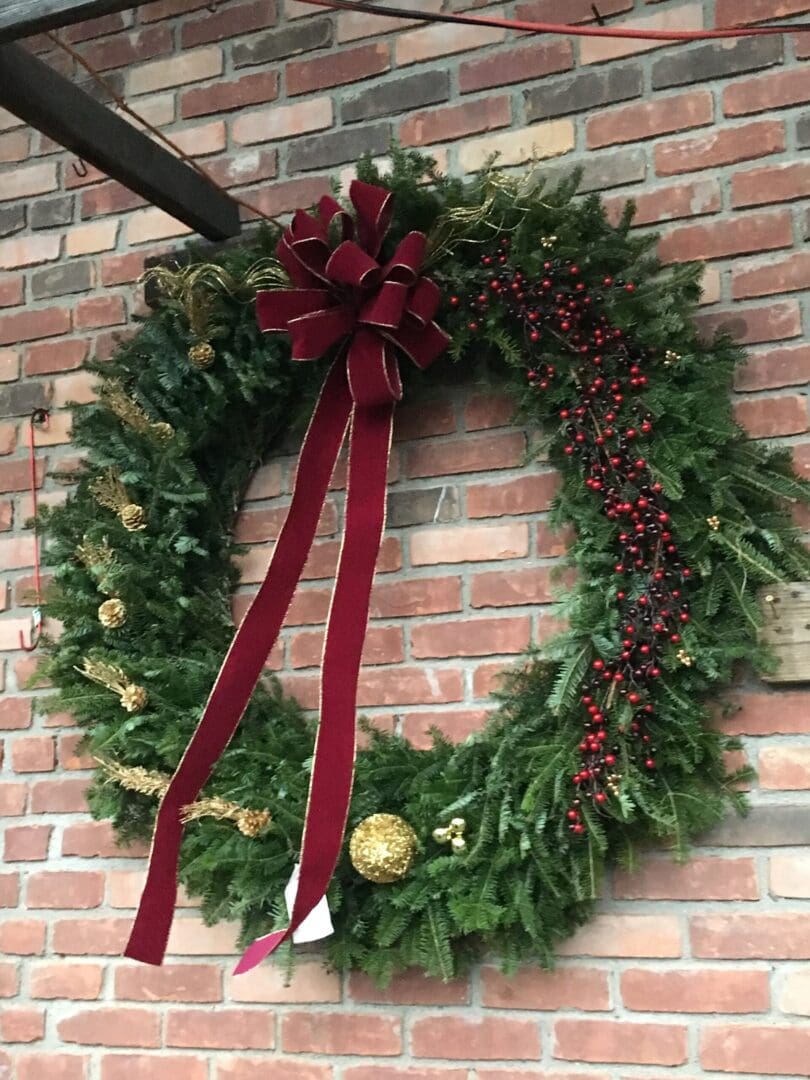 Wreath hanging on a brick wall, adorned with a red ribbon and other decorative items