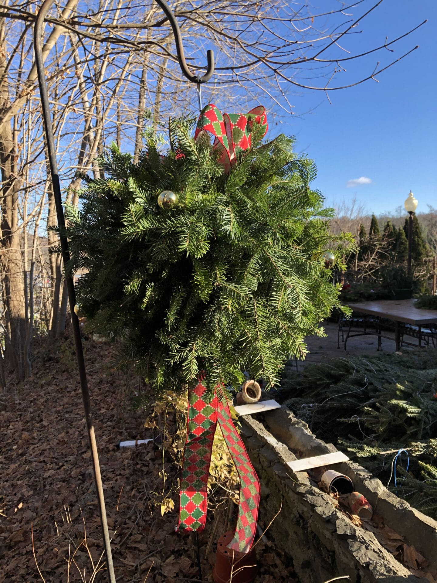 Christmas tree with a red and green bow hanging from a metal pole in the foreground, surrounded by a wall