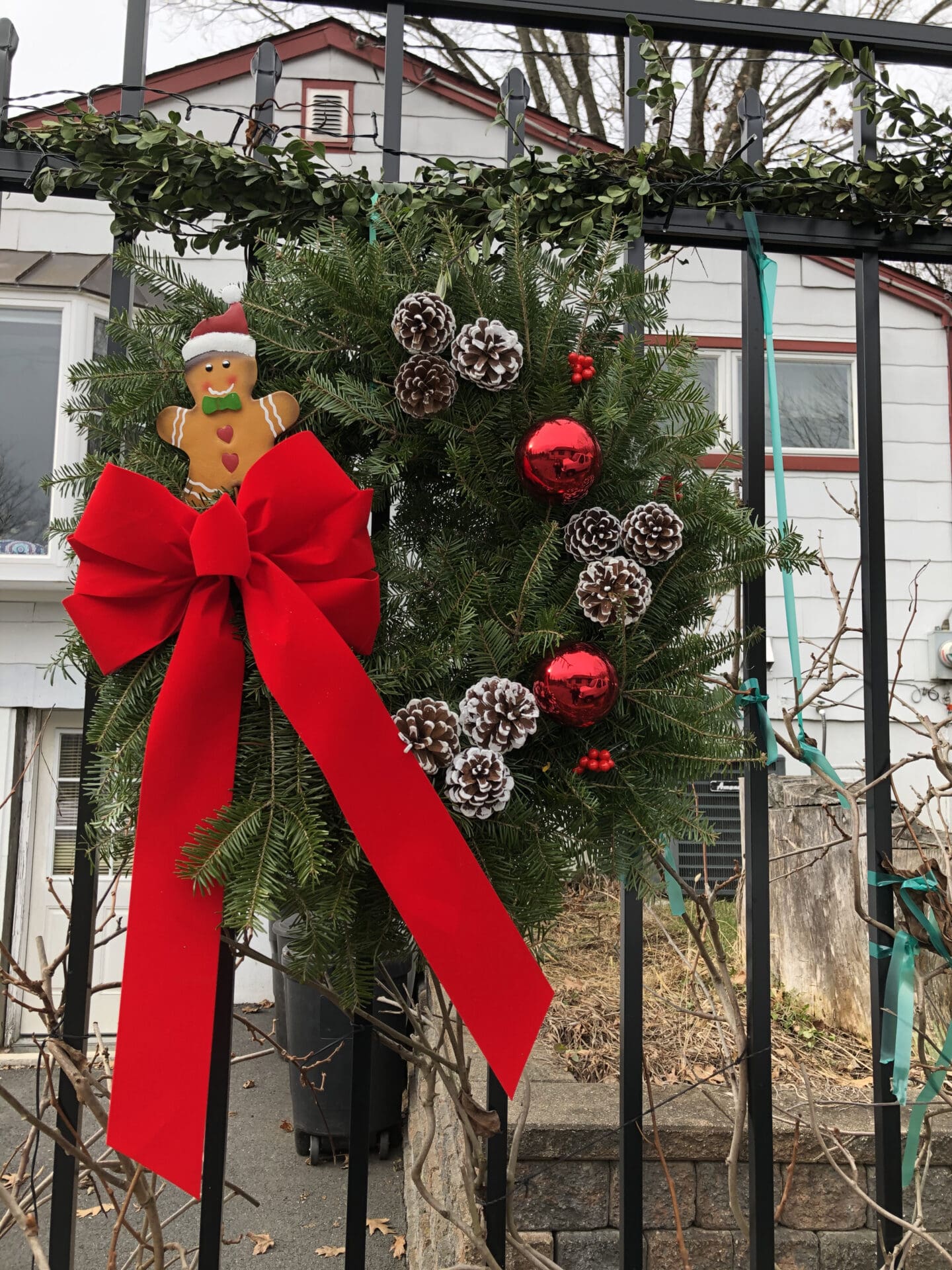 Wreath with a red bow and a gingerbread man on it, hung on a gate in front of a house