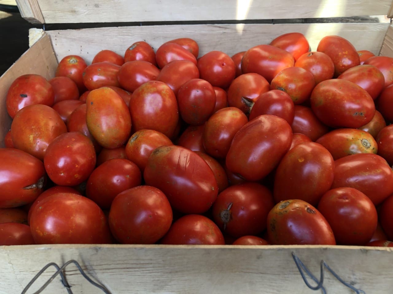 Wooden box filled with lots of red tomatoes sitting on top of a table